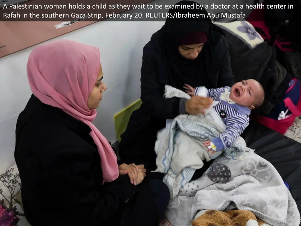 a palestinian woman holds a child as they wait