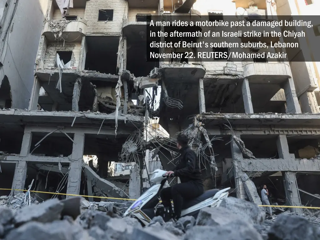 a man rides a motorbike past a damaged building