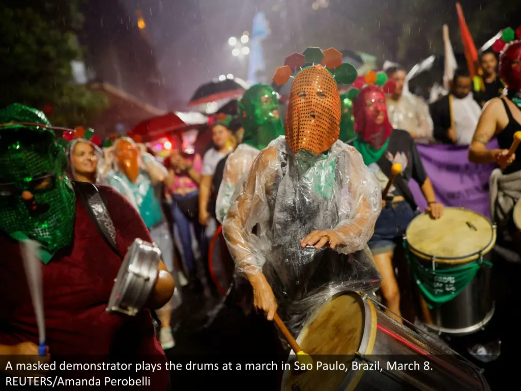 a masked demonstrator plays the drums at a march