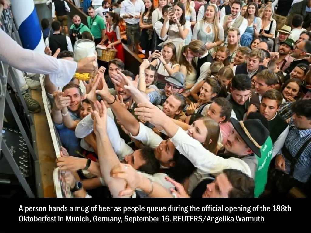 a person hands a mug of beer as people queue